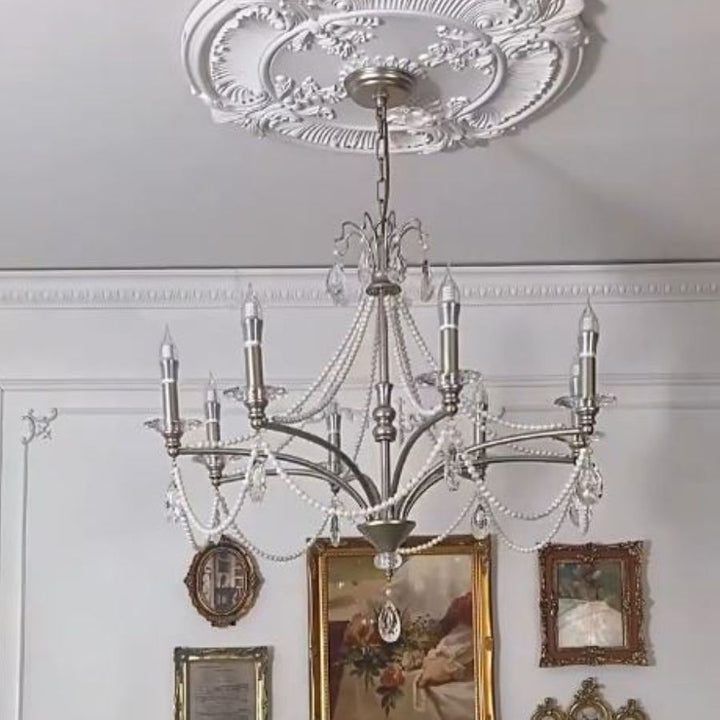 Lustre argenté à pampilles de cristal et bras en volutes, dans un intérieur ancien aux moulures ornementales.