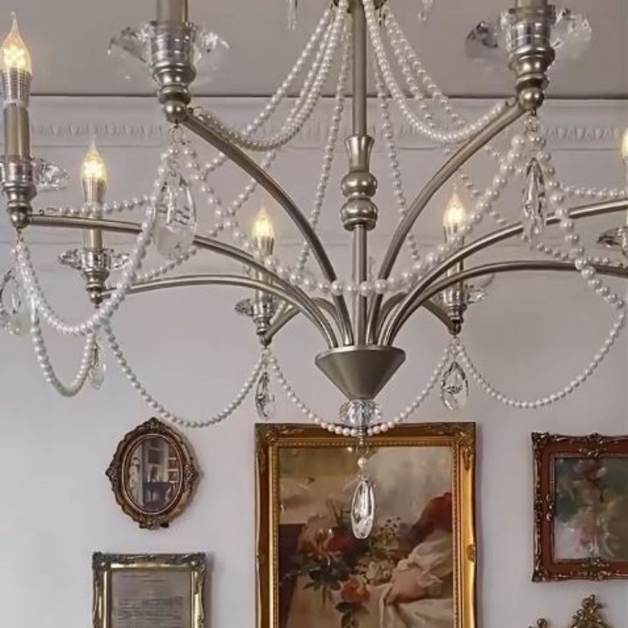 Gros plan sur un lustre argenté de style vintage, aux bras métalliques courbés et guirlandes de perles et cristal.