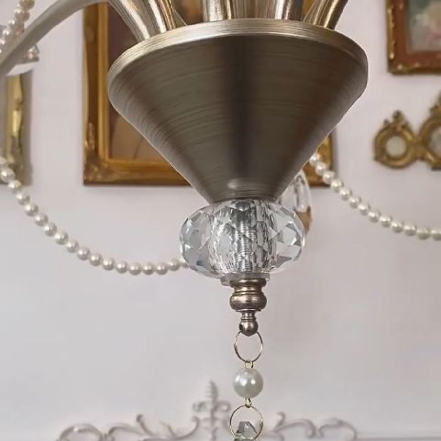 Détail de la finition métal brossé d'un lustre argenté classique, avec élément en cristal facetté et perles nacrées.