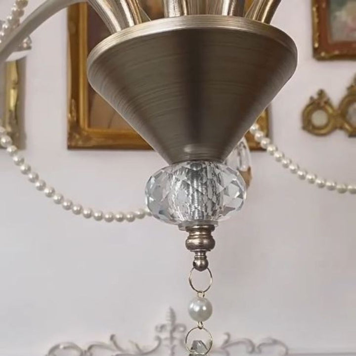 Détail de la finition métal brossé d'un lustre argenté classique, avec élément en cristal facetté et perles nacrées.