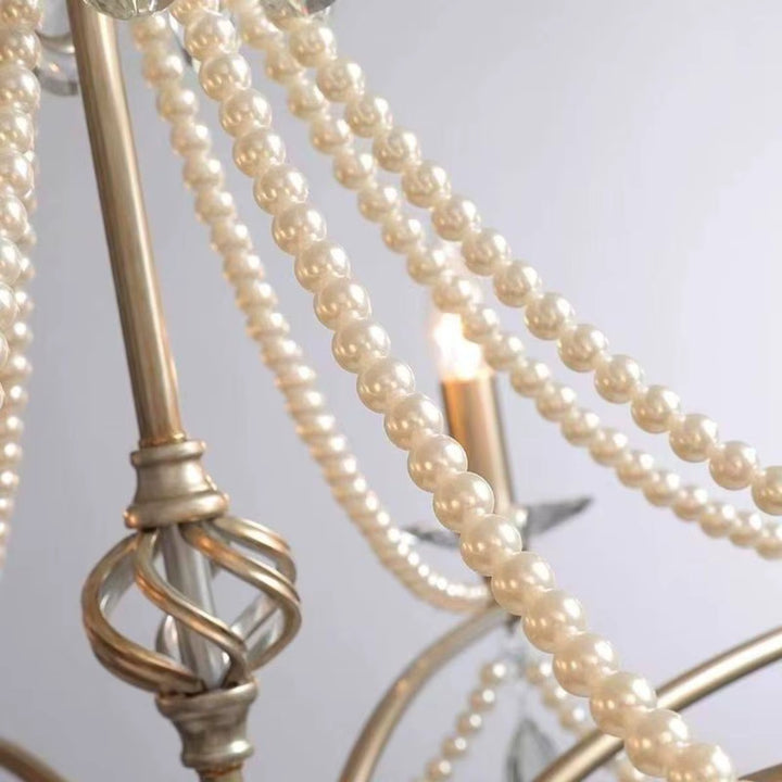 Gros plan sur les guirlandes de perles nacrées et les ornements métalliques d'un lustre argenté au charme rétro.