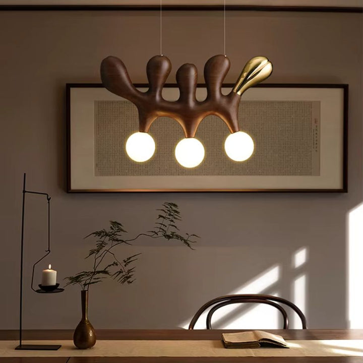 Au-dessus d’une table épurée, ce lustre en bois foncé à trois globes s’intègre dans un décor japandi