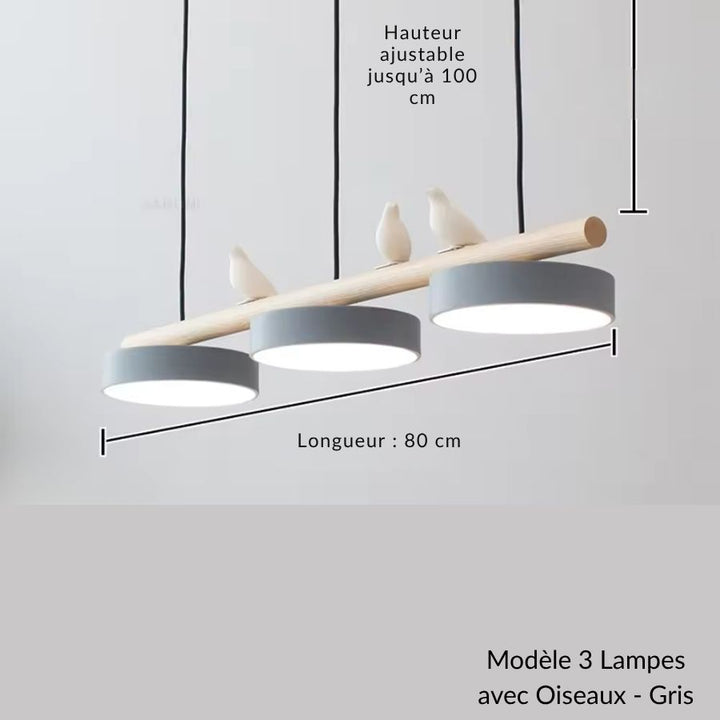 Des oiseaux blancs perchés sur le bois dominent trois disques gris dans ce lustre scandinave au dessin épuré