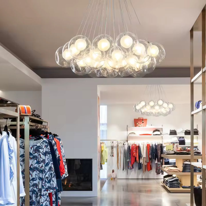 Une grappe de sphères lumineuses en verre transparent forme un lustre sculptural au-dessus d'une boutique de vêtements.