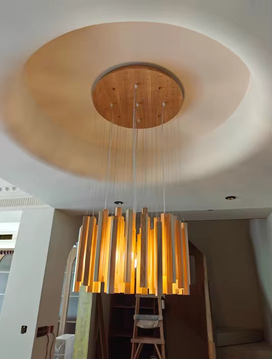 Lustre cascade en bois massif au style Japandi, composé de tasseaux suspendus et baigné d’une lumière chaleureuse