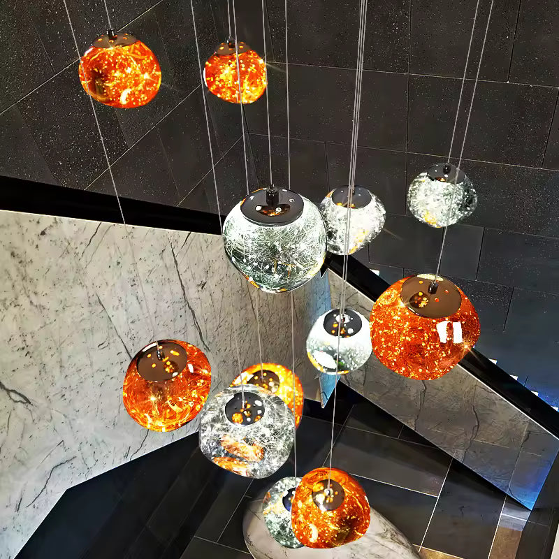Vue plongeante sur un lustre design à globes ambrés et argentés, disposés en cascade dans un escalier en marbre moderne.
