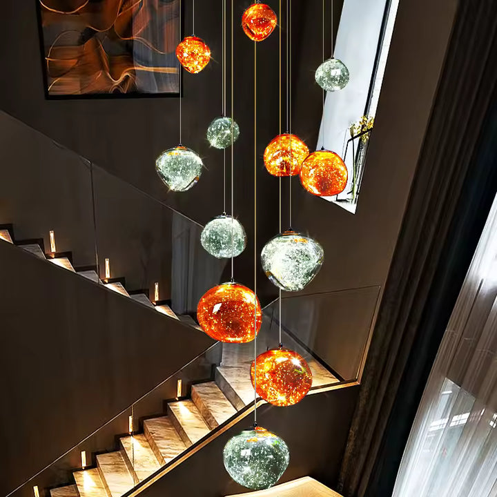 Lustre cascade de globes ambrés et argentés suspendus à différentes hauteurs dans une cage d'escalier au style moderne.