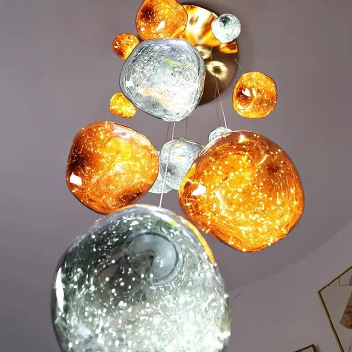 Vue de dessous d'un lustre sculptural aux globes ambrés et argentés texturés, suspendus sous une rosace dorée brillante.