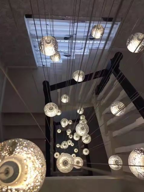 Lustre cascade lumineuse en verre texturé type cristal, composition sculpturale idéale pour escalier et grand volume contemporain.
