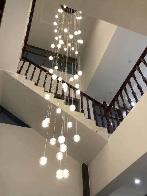 Lustre cascade de sphères en verre pour cage d’escalier, éclairage monumental design et plafond très haut.