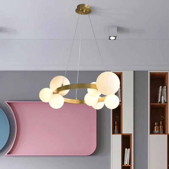 Suspendu devant un décor rose et gris, ce lustre doré à anneau et globes opalins apporte une touche rétro chic.