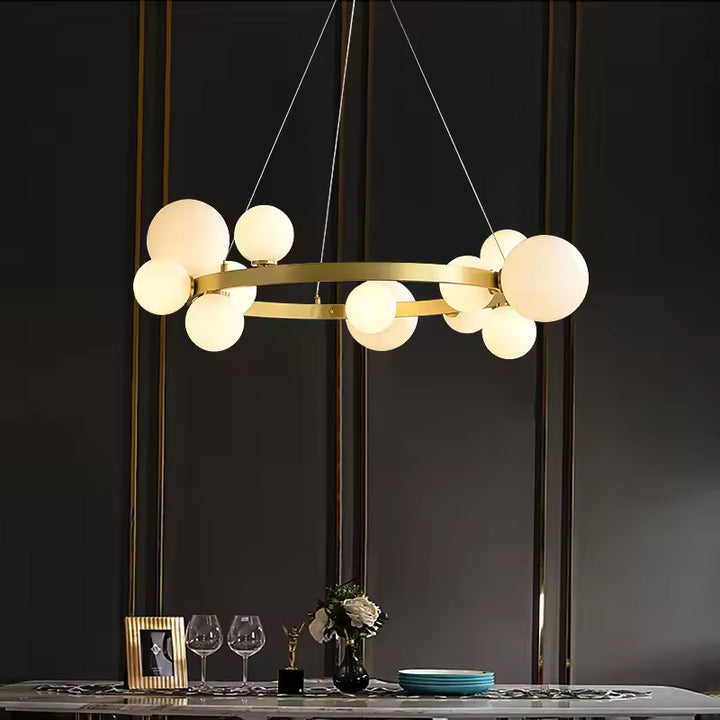 Face à un mur sombre, un lustre circulaire doré aux globes lumineux en verre opalin habille une salle à manger Art déco.