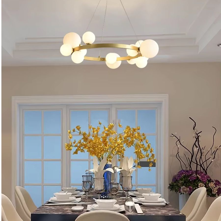 Un lustre doré à globes en verre opalin surplombe une table dressée dans une salle à manger lumineuse au style chic et moderne.