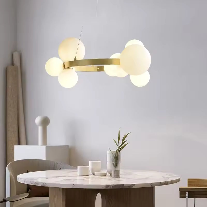 Au-dessus d'une table ronde en marbre, un lustre doré à globes opalins illumine une salle à manger au design minimaliste.