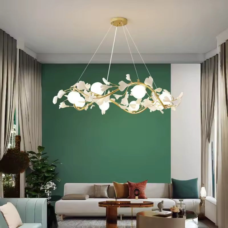 Face à un mur vert, lustre circulaire aux branches dorées, fleurs blanches et globes opalins dans un salon contemporain.