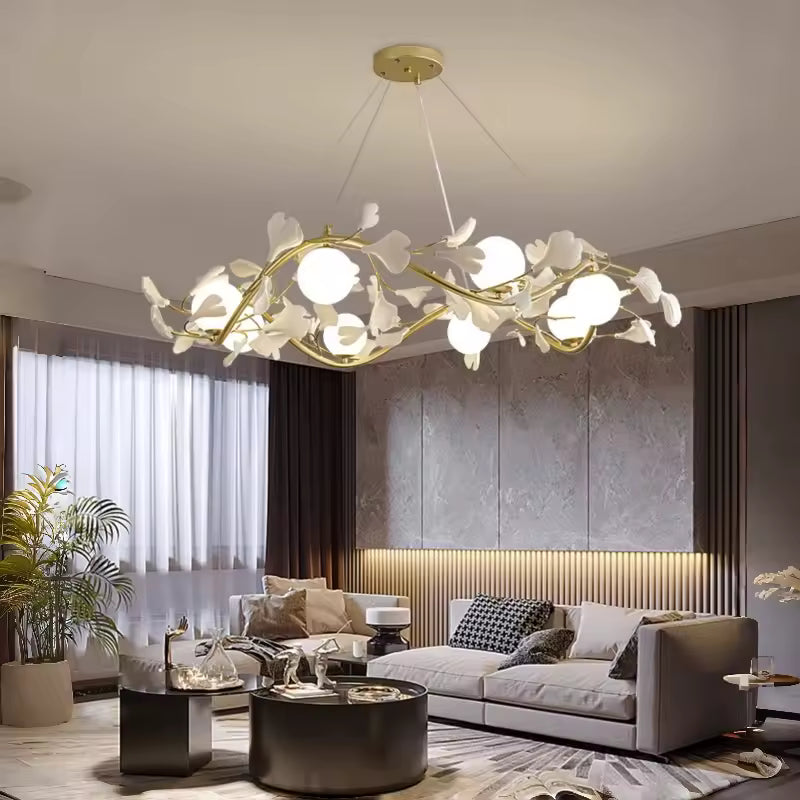 Un lustre floral aux branches dorées et globes opalins illumine un salon moderne avec canapé gris et décoration raffinée.