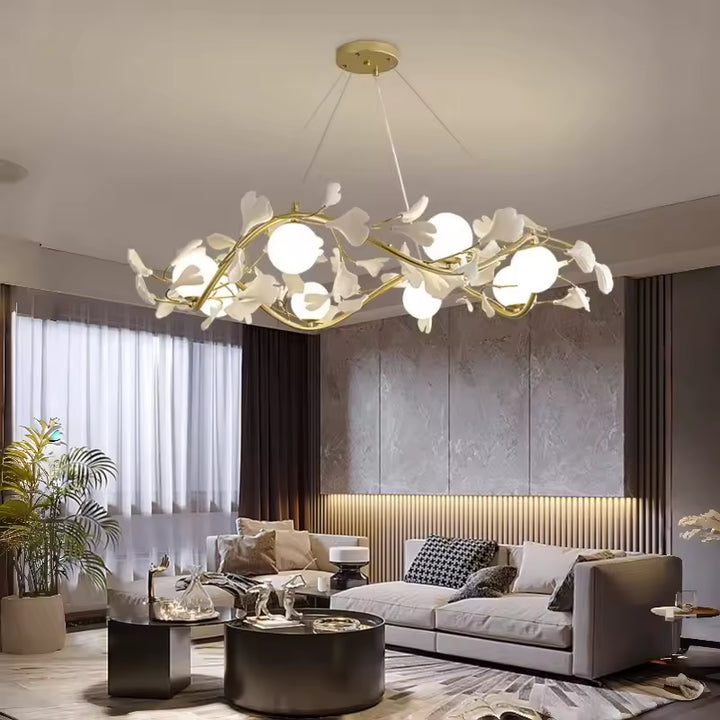Un lustre floral aux branches dorées et globes opalins illumine un salon moderne avec canapé gris et décoration raffinée.