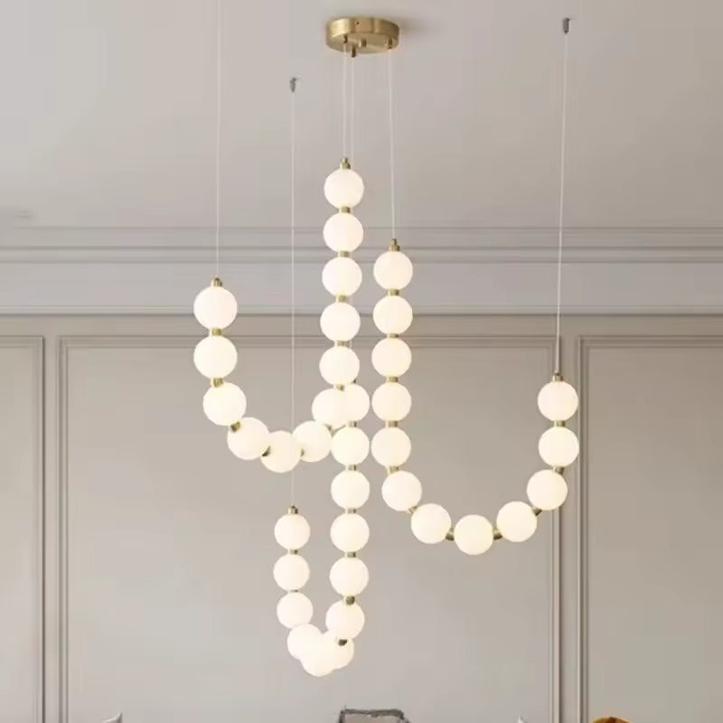 Une cascade de globes lumineux blancs ponctués de doré forme un lustre sculptural au style organique et contemporain