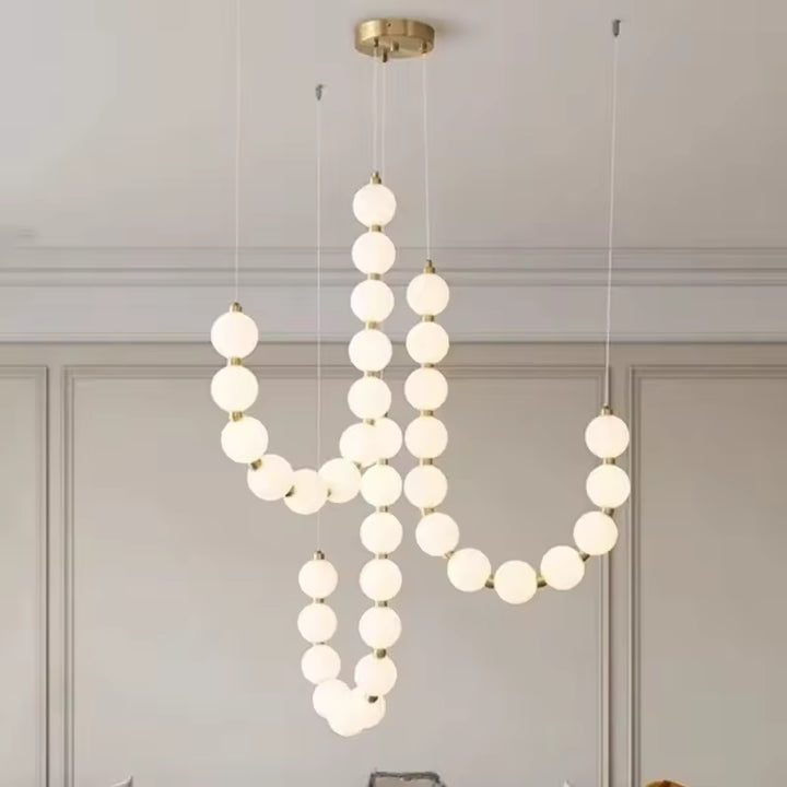 Une cascade de globes lumineux blancs ponctués de doré forme un lustre sculptural au style organique et contemporain