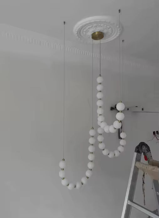 En cours d’installation, ce lustre à globes lumineux blancs révèle sa structure suspendue au style sculptural