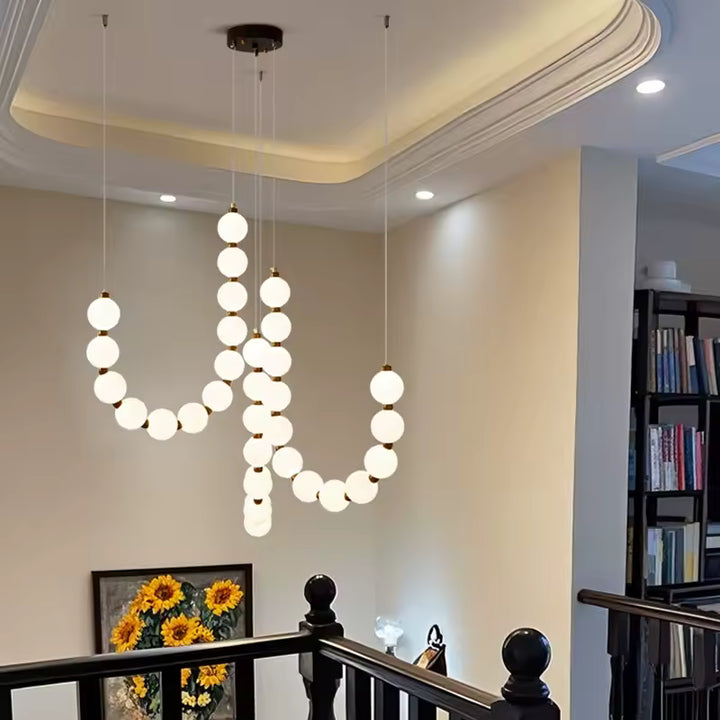 Suspendu au-dessus d’une mezzanine, ce lustre de globes blancs et dorés apporte une touche élégante et contemporaine