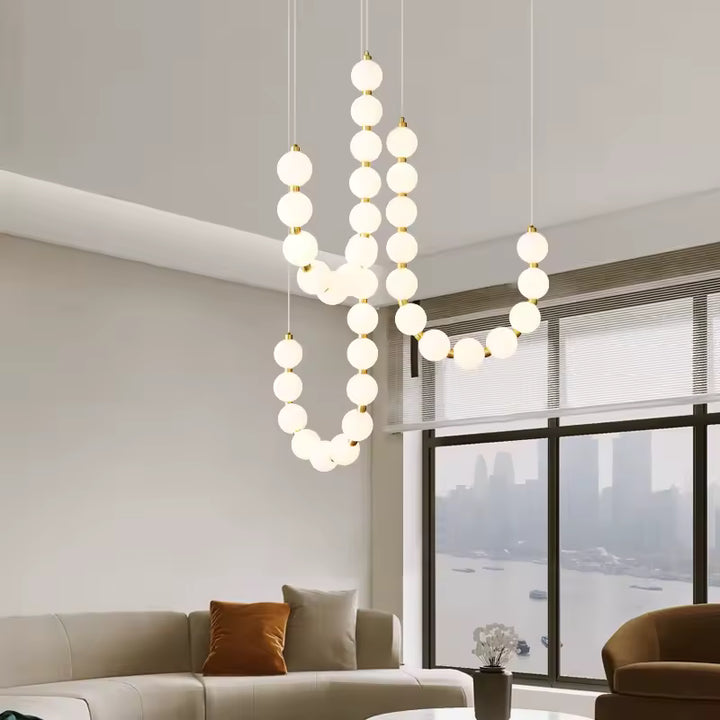 Face à une grande baie vitrée, ce lustre de globes lumineux blancs et dorés apporte un style organique et aérien