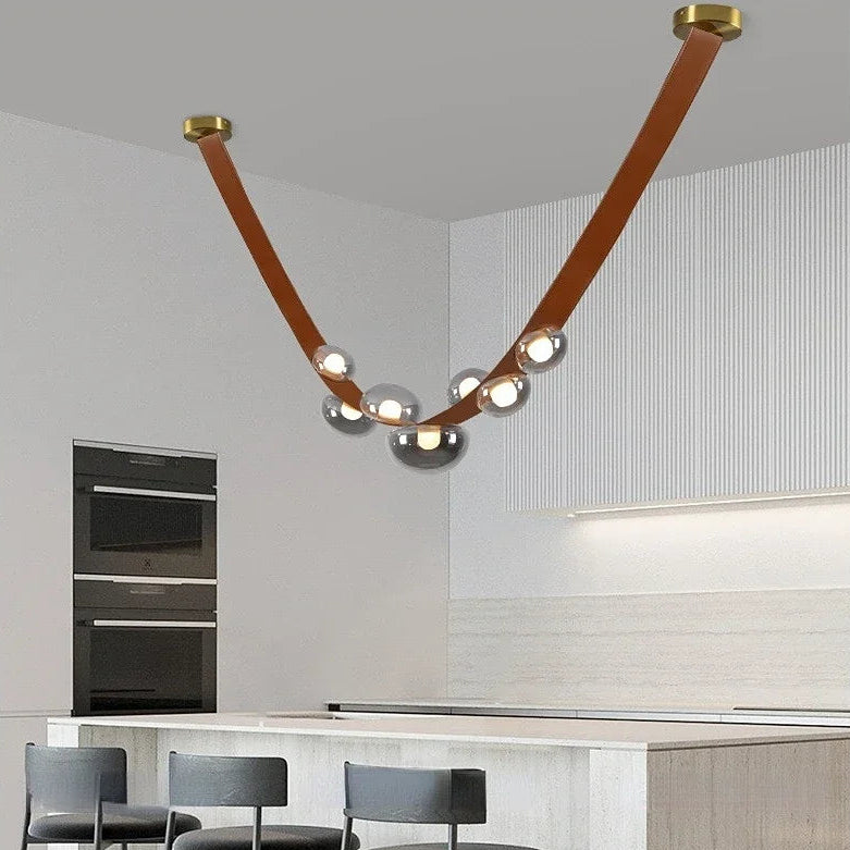 Lustre design en cuir et globes lumineux fumé suspendu au-dessus du îlot central d'une cuisine ouverte.