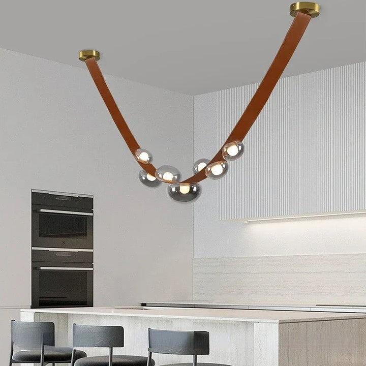 Lustre design en cuir et globes lumineux fumé suspendu au-dessus du îlot central d'une cuisine ouverte.