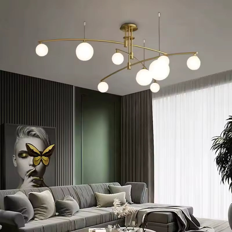 Élégant lustre sculptural doré à bras entrecroisés et globes lumineux en verre blanc, dans un salon moderne raffiné.