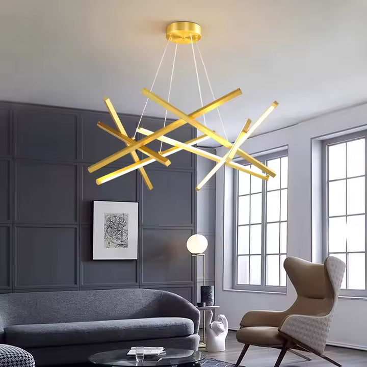 Suspendu dans un salon élégant aux murs gris, ce lustre doré aux barres LED croisées affirme un style sculptural et raffiné.