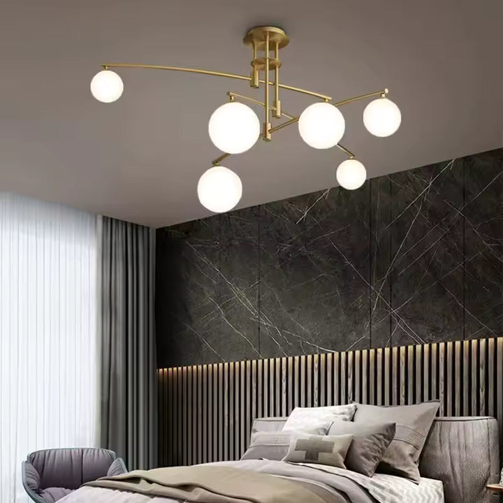 Au-dessus d'un lit, lustre doré aux bras déployés et globes en verre opalin, mêlant élégance moderne et esprit rétro.