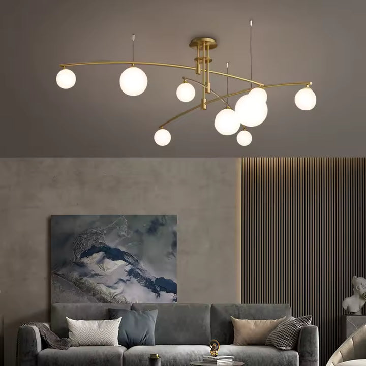 Au plafond d'un salon épuré, lustre doré à bras métalliques asymétriques et sphères lumineuses au style moderniste.