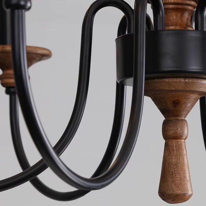 Détail des bras métalliques noirs galbés et du bois brun sculpté d'un lustre en bois ancien au charme rustique.