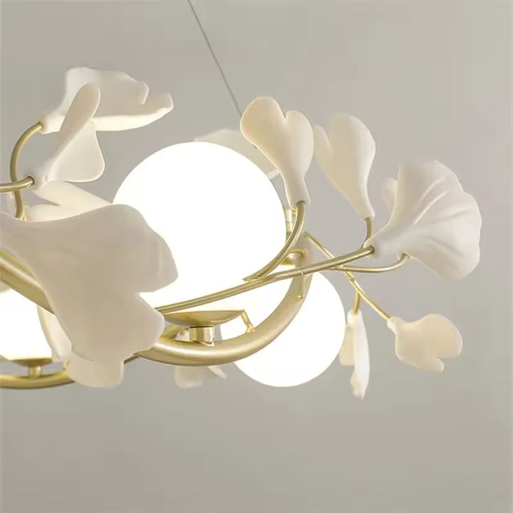 Gros plan sur les fleurs blanches sculptées et les globes opalins lumineux d'un lustre doré au style Art déco revisité.
