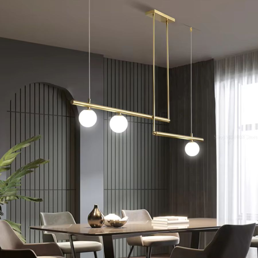 Lustre doré à trois globes opalins et lignes décalées, suspendu au-dessus d’une salle à manger contemporaine