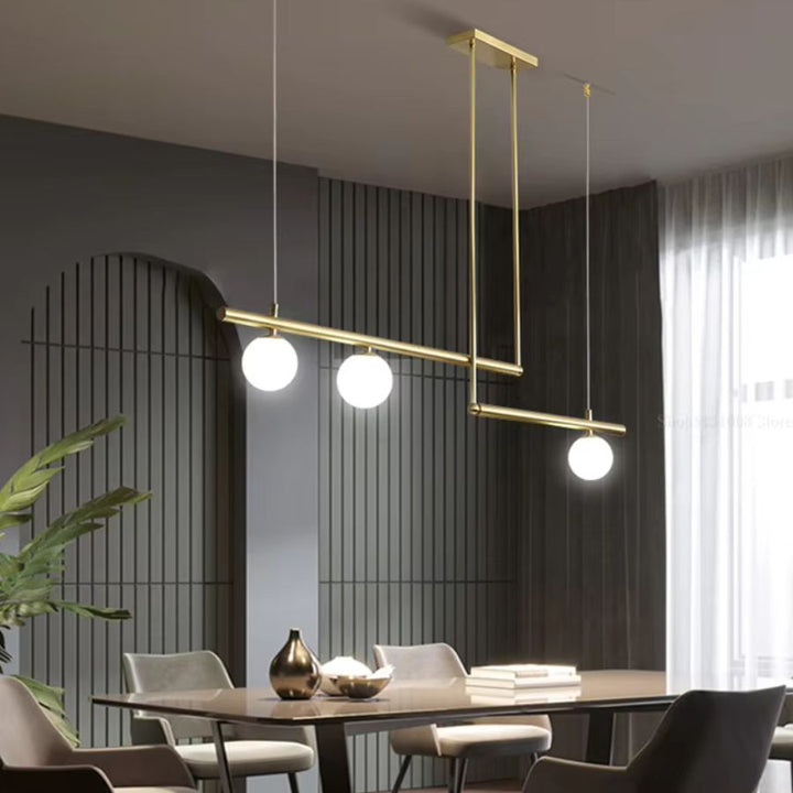 Lustre doré à trois globes opalins et lignes décalées, suspendu au-dessus d’une salle à manger contemporaine