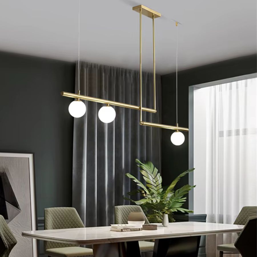 Lustre doré à structure géométrique décalée et trois globes opalins, au-dessus d’une salle à manger élégante