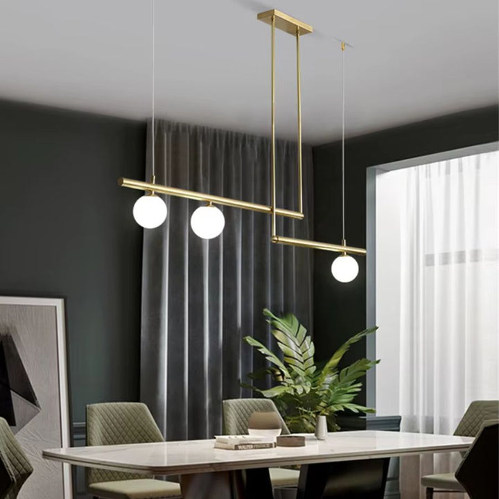 Lustre doré à structure géométrique décalée et trois globes opalins, au-dessus d’une salle à manger élégante