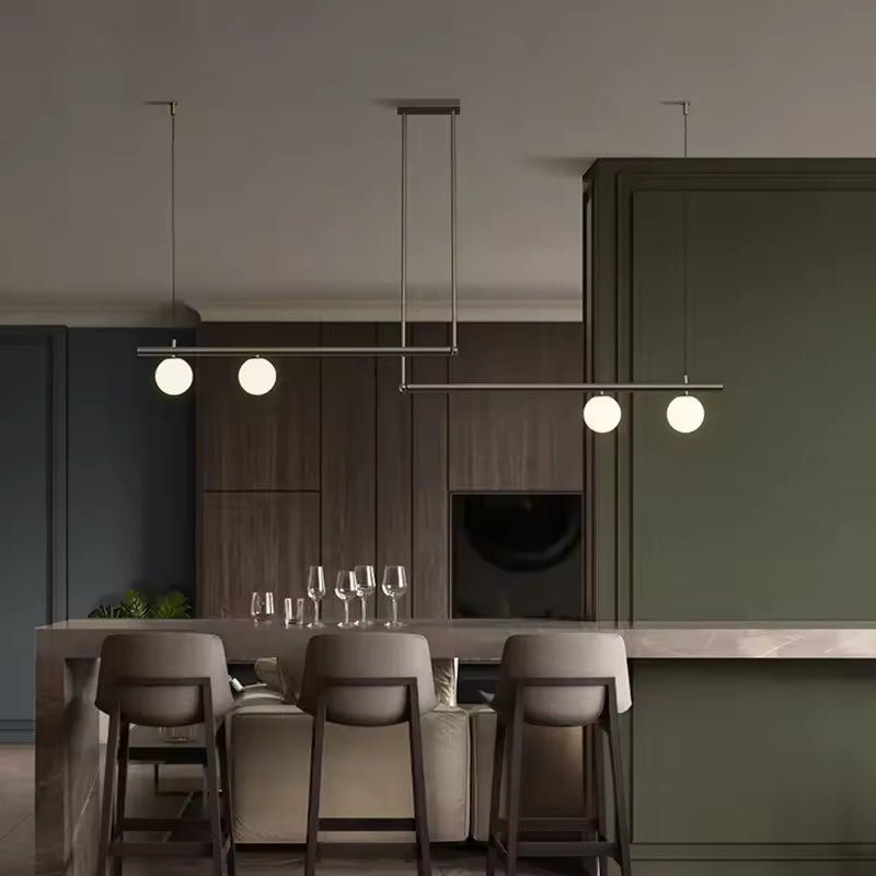 Lustre noir à lignes décalées et quatre globes opalins, suspendu au-dessus d’un îlot dans une cuisine design