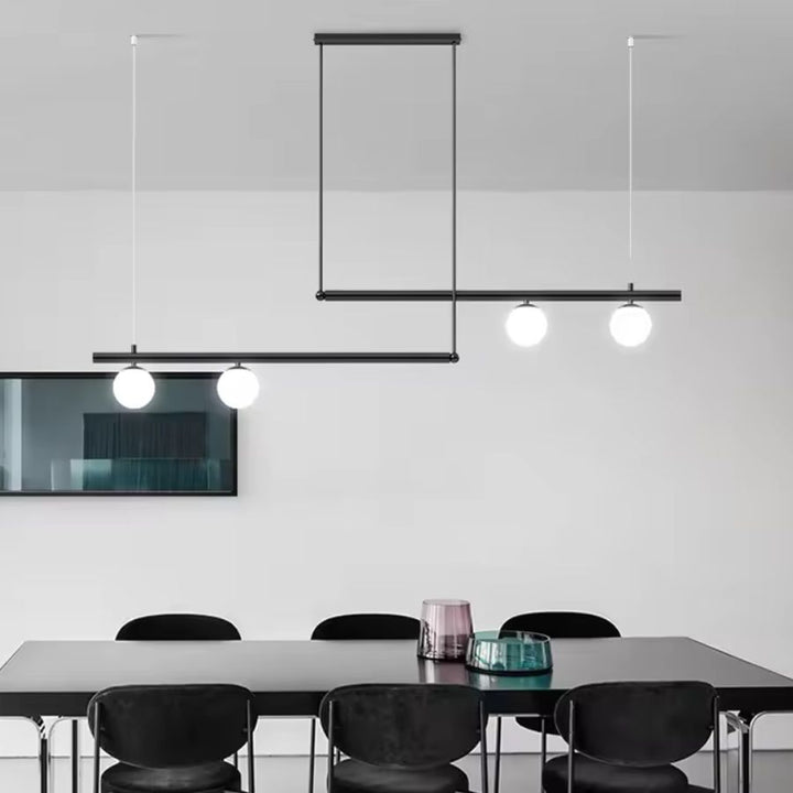 Lustre noir à structure décalée et quatre globes opalins, soulignant une salle à manger au design graphique et moderne