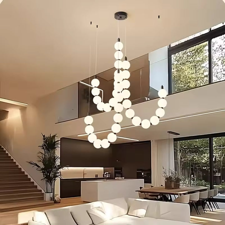 Dans cet intérieur à plafond haut, le lustre de globes lumineux crée une présence aérienne, moderne et sculpturale