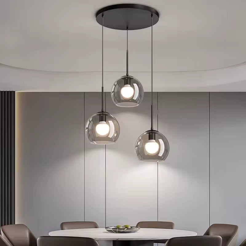 Dans la salle à manger, trois globes en verre fumé suspendus à différentes hauteurs créent un lustre moderne