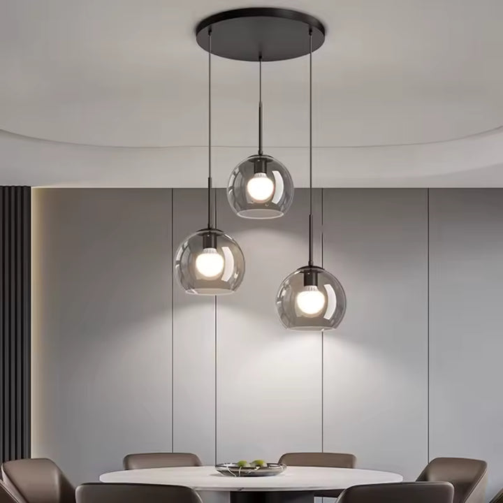 Dans la salle à manger, trois globes en verre fumé suspendus à différentes hauteurs créent un lustre moderne