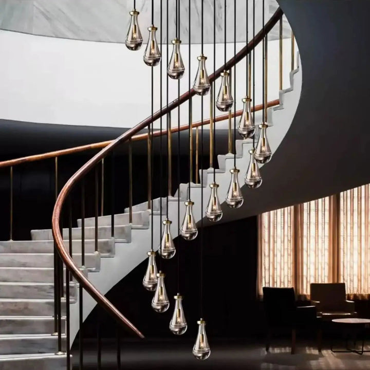 Lustre majestueux en verre et cuivre, composé de gouttes d'eau, illuminant harmonieusement une cage d'escalier.