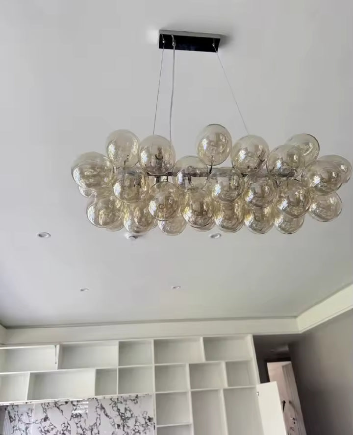 Sous un plafond clair, ce lustre grappe linéaire en verre champagne affiche un design aérien et contemporain