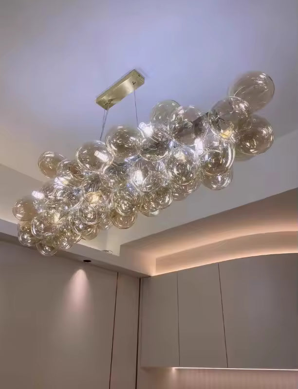 Vue en contre-plongée d’un lustre grappe linéaire en verre champagne au design lumineux, organique et contemporain