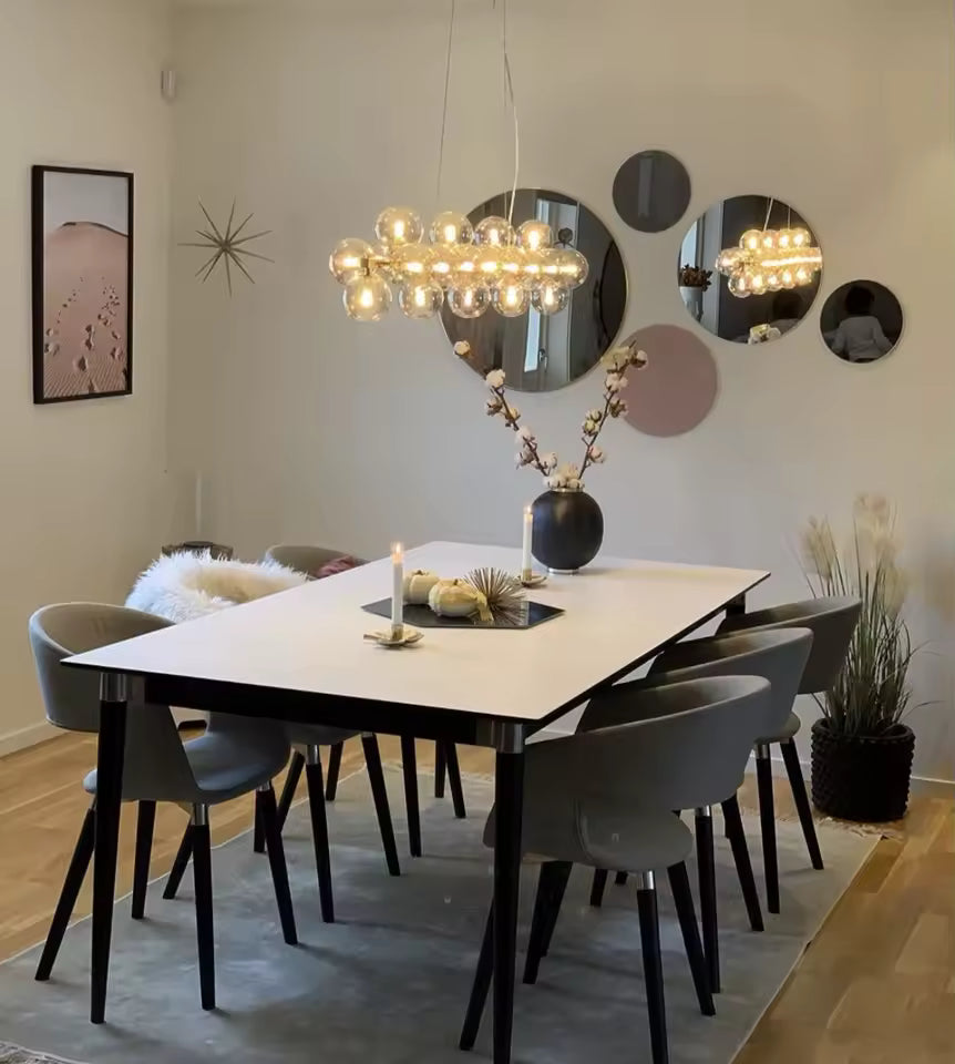 Dans une salle à manger design, ce lustre grappe linéaire en verre champagne diffuse une lumière chaleureuse et élégante