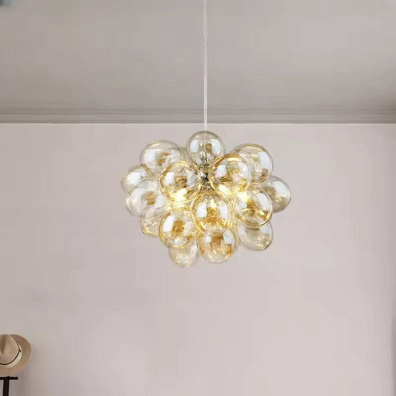 Avec ses bulles en verre champagne, ce lustre grappe diffuse un style lumineux, élégant et organique