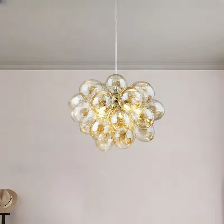 Avec ses bulles en verre champagne, ce lustre grappe diffuse un style lumineux, élégant et organique