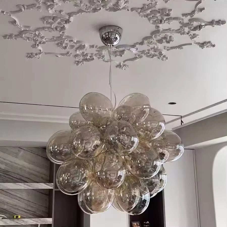 Sous un plafond ornementé, ce lustre grappe en verre champagne révèle un volume sculptural, élégant et contemporain